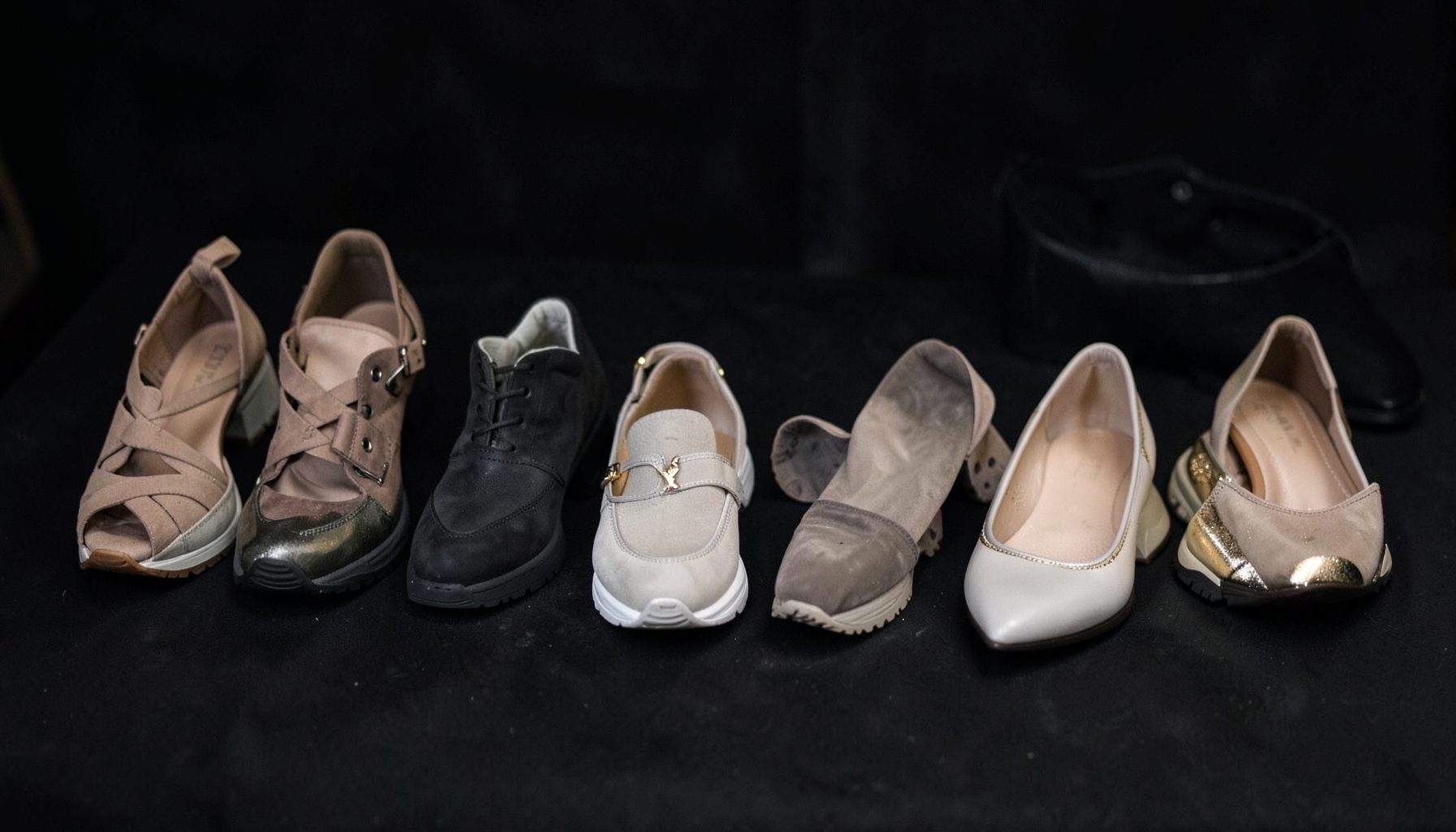 A row of stylish women's shoes on a dark surface — strappy heels, chunky sneakers, and sleek flats in neutral tones