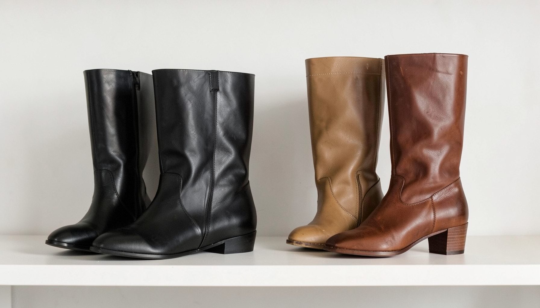 Ankle boots and knee-high boots in black and tan leather-look finishes arranged on a minimalist shelf