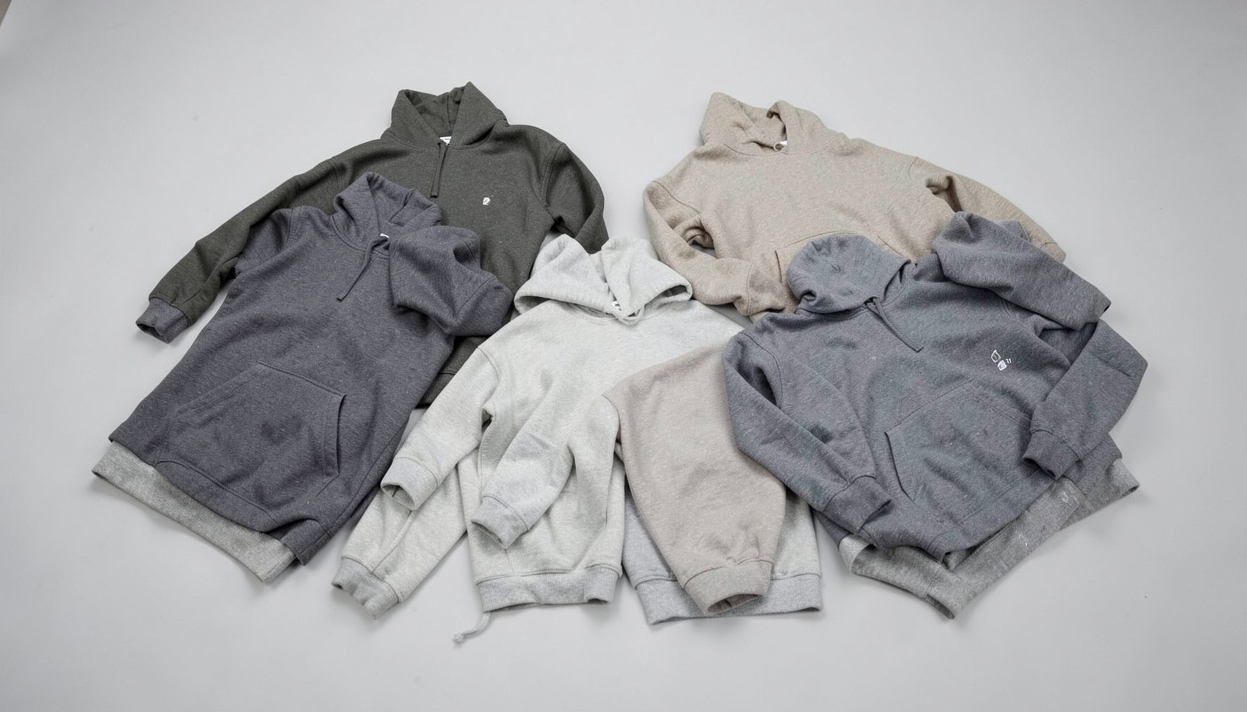 Coordinated joggers and hoodies in muted tones laid out on a light gray studio surface