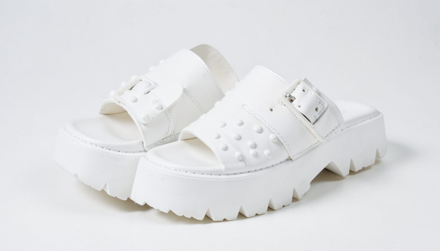 White flatform studded double-buckle mule slides with chunky soles on a clean studio surface